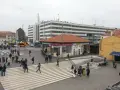 Persone attraversano una piazza a Venezia, con autobus e un edificio moderno sullo sfondo.