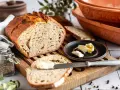 Ein rustikales Roggenbrot mit Sauerteig, aufgeschnitten und mit Butter bestrichen. Daneben ein Glas Kümmel und ein Messer.