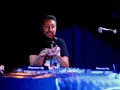 Un dj hip hop souriant, mains en l'air, mixe sur scène devant un public invisible.