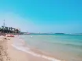 Słoneczne bari plaże z turkusową wodą, palmami i miastem w tle. Czerwona łódź ratownicza czeka na plaży.