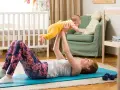 Frau macht Beckenbodentraining mit Baby. Sie liegt auf einer Matte und hebt ihr Kind hoch.