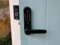 Nimly Touch Pro test: Svart digital dörrlås med kodpanel och fingeravtrycksläsare monterat på en ljusblå dörr. Bredvid syns en Ring-ringklocka.