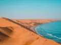 Piaskowe wydmy Namibii spotykają się z turkusowym oceanem. Idealna namibia pogoda na podziwianie tego kontrastu.