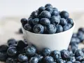 Un bol de myrtilles débordant, certaines tombées sur la table. Attention, ces petites baies bleues peuvent être addictives !