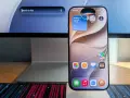 Ein iPhone zeigt Widgets für Wetter, Uhr und Kamera. Die Frage "was kann Siri alles" wird durch die vielen Apps und die Suchleiste auf dem iMac im Hintergrund angedeutet.