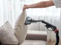 En person använder en soffdammsugare för att rengöra en ljusbeige kudde på en soffa.