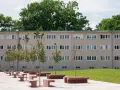 Nowoczesny budynek mieszkalny w stylu wuwa Wrocław z rzędem drzew i betonowych ławek przed fasadą.