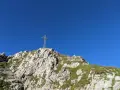 Widok na szczyt Giewontu z krzyżem i błękitnym niebem. W oddali widać samolot.