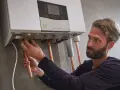 Installazione di una caldaia. Si sente il rumore dell'acqua che scorre mentre un tecnico collega i tubi di rame.