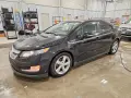 Czarny Chevrolet Volt stoi w garażu, mokry od deszczu. W tle regały z narzędziami i drabina.