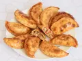 Empanadas de carne doradas y crujientes en un plato, una partida muestra el relleno.
