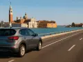 Un'auto grigia percorre il ponte verso Venezia, con la Basilica di San Giorgio Maggiore e il campanile che si stagliano sullo sfondo.