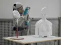 A person in a protective suit sprays a white 3D printed bust and torso, demonstrating how to paint 3d prints for a smooth finish.