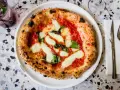 Pizza Margherita: darauf sind Tomatensauce, Mozzarella und frische Basilikumblätter.