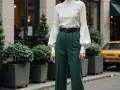 Elegancka kobieta w zielonych spodniach z wysokim stanem i bufiastymi rękawami, przypominającymi kształtem **stovepipe**.