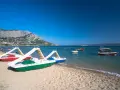 Plaża z łódkami i zjeżdżalniami, idealna na wakacje w camping Galeb. W tle góry i turkusowe morze.