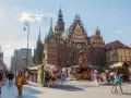 Tłum ludzi spaceruje po starym rynku we Wrocławiu, podziwiając piękną architekturę i letnie stoiska.