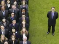 Grupa ludzi w garniturach, tworząca linię. Jeden mężczyzna stoi osobno, co to jest korporacja?