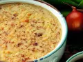 Una ricca zuppa di cipolle gratinata, con crostini dorati e formaggio fuso. Accanto, una cipolla rossa e foglie verdi.