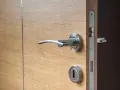 Maniglia e serratura di una porta in legno chiaro, con un'ombra scura che suggerisce una porta che cigola.