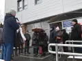 Grupa ludzi stoi przed budynkiem spółdzielni mieszkaniowej w deszczu, niektórzy pod parasolem.