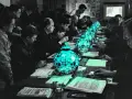 Des hommes en costume, réunis autour d'une longue table, semblent participer à un procès de Tokyo. Des lampes bleues éclairent des documents.