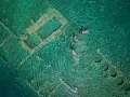 Swimmers explore the sunken city of Epidaurus, its ancient stone structures visible beneath the clear turquoise water.