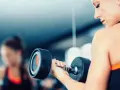 Frau hebt Hantel. Die Frage, wieviel kg darf eine Frau heben arbeitsrecht, ist hier nicht relevant, da es um Fitness geht.