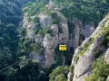 A bright yellow cable car ascends the rugged, tree-covered cliffs of Montserrat, Spain.