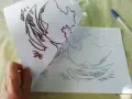 Une main tient une feuille avec un dessin de vague, prête à comment décalquer sur une toile. Un stylo bleu est visible.