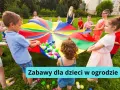 Dzieci bawią się kolorowym spadochronem z piłeczkami w ogrodzie. Radosne kreatywne zabawy w ogrodzie.