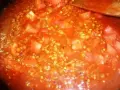 Buchweizen kochen mit Tomaten. Ein Holzlöffel rührt in der roten Sauce mit den Buchweizenkörnern und Tomatenstücken.