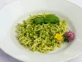 Pasta al pesto con hojas de albahaca fresca y flores comestibles.