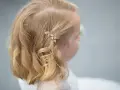 Urocze fryzury ze spinką z boku, ozdobioną złotymi listkami, dodają blasku blond włosom dziewczynki.