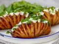Pieczone ziemniaki Hasselback z bekonem, majonezem i szczypiorkiem na talerzu.