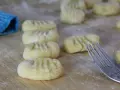 Frisch geformte Gnocchi liegen auf bemehltem Holz. Eine Gabel und ein blauer Lappen deuten auf die Zubereitung von Gnocchi Rezepten hin.