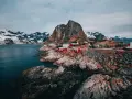 Röda fiskestugor vid en klippig kust med snöklädda berg i bakgrunden. En av de fina platserna i Norge.