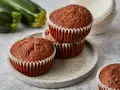 Saftige zucchini schoko muffins auf einem Steinplattenteller, im Hintergrund frische Zucchini.