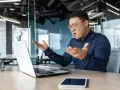 Mężczyzna w okularach gestykuluje, wyrażając frustrację. Czyżby jego słabe cechy charakteru dały o sobie znać podczas wideokonferencji?