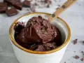 Ein Schöpfer holt cremiges Schokoladeneis aus einer Eismaschine. Dunkle Schokostückchen zieren die köstliche Masse.
