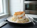 Dos lomos de bacalao a la gallega, dorados y jugosos, reposan sobre una cama de cebolla pochada en un plato blanco.
