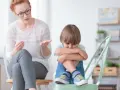 Nauczyciel wspomagający z troską rozmawia z chłopcem, który skulony siedzi na krześle.