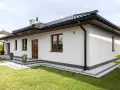 Nowoczesny biały dom z brązowymi oknami i drzwiami, otoczony zielonym trawnikiem.