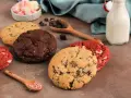 Verschiedene amerikanische Cookies: Schoko, Red Velvet und Chocolate Chip. Dazu Marshmallows, Schokostückchen und Milch.