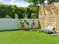 Terraza con césped artificial verde vibrante, plantas en macetas, un banco y una valla de madera.