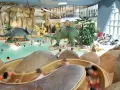 Kinder planschen im Dino-Bad, ein perfektes Ziel für die Herbstferien in Hamburg. Rutschen und Dinosaurier sorgen für Spaß.