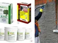 Applicazione di intonaco interno con pistola. Si vedono sacchi e secchi di prodotti per intonaci a base di calce, con indicazioni sullo spessore intonaco interno.