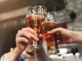 Trzy ręce unoszą kieliszki ze złotym piwem, tworząc toast. Każde piwo w szklance wygląda apetycznie.