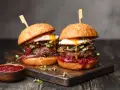 Zwei saftige Burger mit Spiegelei, Pilzen und roten Zwiebeln, serviert auf einem Holzbrett. Ein Muss für jeden Burger Laden in Berlin.