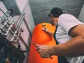 Technik sprawdza temperaturę na dużym, pomarańczowym bojlerze. System ogrzewania gazowego jest w pełni sprawny.